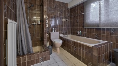 Badeværelse med smalt brusehjørne, badekar og gulvstående toilet