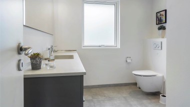 Badeværelse med væghængt toilet og gråt badeværelsesmøbel