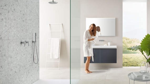 En kvinde tørrer sit hår med et håndklæde i et badeværelse med åben bruser og store fliser i terrazzo-stil