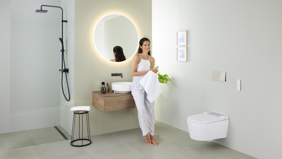 Kvinde læner sig op ad en håndvask i et badeværelse med Geberit AquaClean Sela douchetoilet og Geberit VariForm håndvask og badeværelsesmøbler