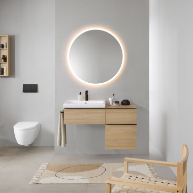Et badeværelse med grå vægge, Geberit badeværelsesmøbler af træ og et rundt Geberit Option spejl med lys